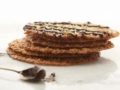 a stack of cookies sitting on top of a white table next to a spoon and chocolate