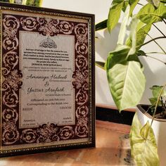 an ornate wedding card on a table next to a potted plant and other plants