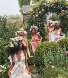 three women in dresses walking through a garden with flowers on their head and one woman wearing a flower crown