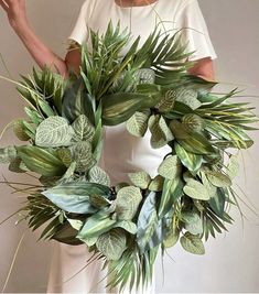 a woman is holding a wreath made out of green leaves and greenery with her hands