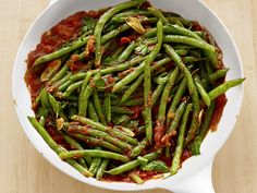 a white bowl filled with green beans covered in tomato sauce on top of a wooden table