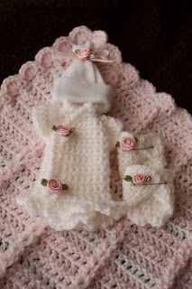 a crocheted baby sweater and booties laying on top of a blanket