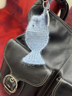 a handbag with a knitted fish on the handle is sitting next to a purse