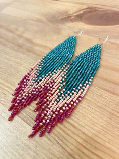 beaded earrings with pink and blue fringes on a wooden table, close up