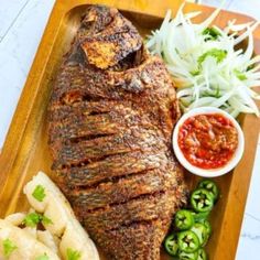 a large piece of meat on a wooden platter with green peppers and sauces