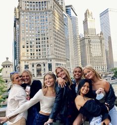 a group of women standing next to each other in front of tall buildings and water