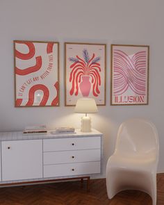 a white chair sitting next to a table with a lamp on it in front of two pictures