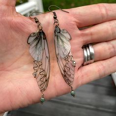 These forest fairy grunge earrings can only be described as enchanting. Measuring 2" in length with a 2.25" drop, they delicately sway, crafted from translucent printed plastic adorned with olive green accents and a subtle dusting of golden glitter, adding a touch of sparkle.An olive green opaque crystal and multi-colored metallic luster crystal dangle from twisted wire branches in your choice of antique bronze or gold. These enchanted fairy wing earrings are suspended on either antique bronze o Enchanted Forest Accessories, Forestcore Accessories, Cool Earings Ideas, Big Funky Earrings, Crowcore Accessories, Crystal Earrings Dangle, Tangled Inspired Jewelry, Nature Themed Jewelry, Fairygrunge Jewelry