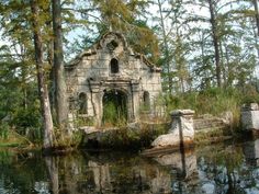 an old building sitting in the middle of a forest next to a body of water