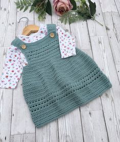 a crocheted baby sweater and shirt laying on top of a wooden floor next to flowers