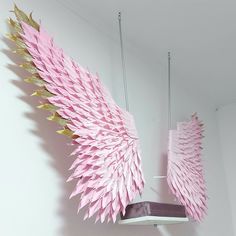 a pink and gold angel wing hanging from a ceiling fixture in a white walled room