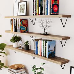 three wooden shelves with books and plants on them in a room next to a white wall