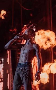 a man with no shirt on standing in front of a stage and holding a microphone