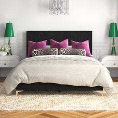 a white bed with pink and purple pillows in a bedroom area next to two green lamps