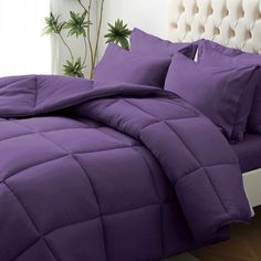 a bed with purple comforter and pillows on it