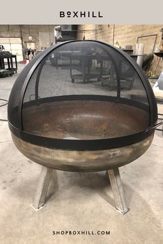 A black lift off dome outdoor fire pit screen mounted on a metal fire bowl placed on a workshop storage area