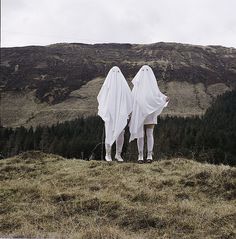 two people in ghost costumes standing on top of a hill