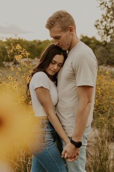 a man and woman standing next to each other in a field with wildflowers