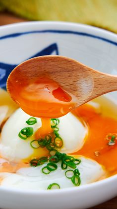 a wooden spoon scooping some food out of a bowl with eggs and green onions