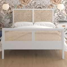 a white bed with wicker headboard and foot board in front of floral wallpaper