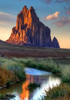 a large rock formation in the middle of a grassy field with water running through it