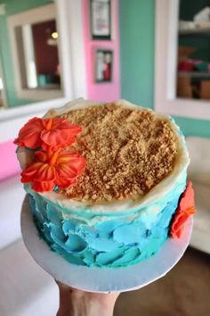 a person holding up a cake with blue frosting and flowers on the top layer