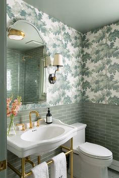 a white toilet sitting next to a sink in a bathroom under a mirror with gold fixtures