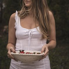 a woman holding a bowl with strawberries in it