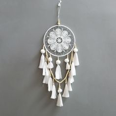 a white doily with tassels and beads hanging from the side on a gray wall