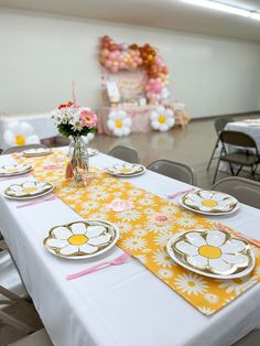 the table is set with yellow and white plates, silverware, and pink flowers