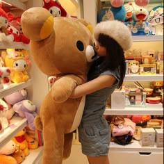 a woman is hugging a large teddy bear in a store with shelves full of stuffed animals