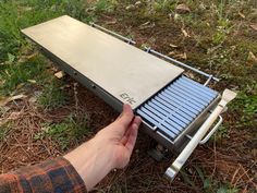 a hand is holding the bottom part of an outdoor grill that has been placed on the ground