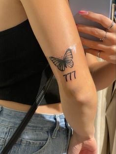 a woman with a butterfly tattoo on her arm holding a cell phone and looking at it