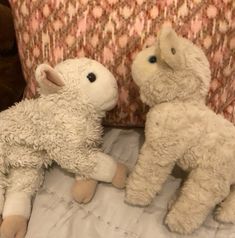 two stuffed animals sitting on top of a bed next to each other, one white and the other light brown