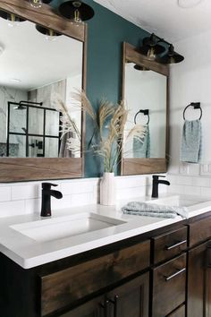 a bathroom with two sinks, mirrors and towels hanging on the wall above it is a plant in a white vase