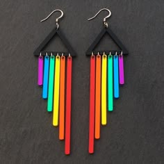 a pair of multicolored earrings hanging from black hooks on a dark surface,