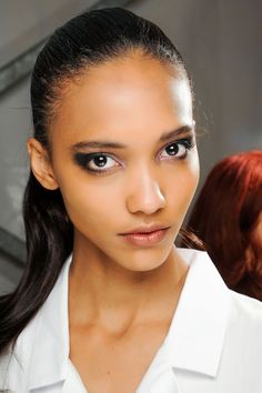 a woman with long hair wearing a white shirt and black eyeliners is looking at the camera