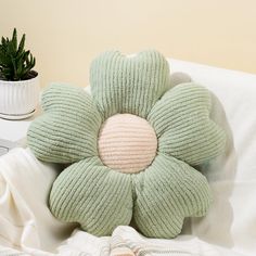 a flower shaped pillow sitting on top of a bed next to a potted plant