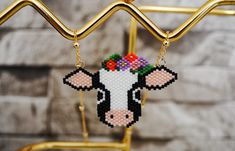 a cross stitch cow with flowers on it's head hanging from a gold bar