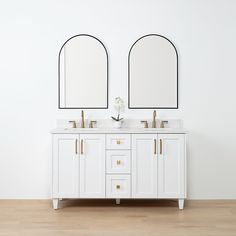 two mirrors on the wall above double sinks in a white bathroom with wood flooring