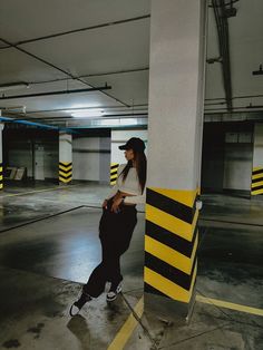 a woman leaning against a pole in an empty parking garage with yellow and black stripes