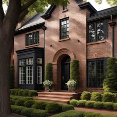 a large brick house with black windows and trimmings on the front door, surrounded by trimmed hedges