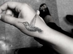 a small hummingbird tattoo on the left wrist and right hand is shown in black and white