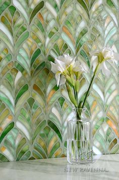 two white flowers in a glass vase against a wall with green and yellow mosaic tiles