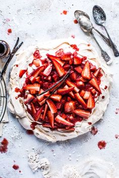 a pie with strawberries and whipped cream on top, next to utensils