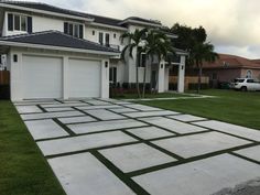 a driveway with grass in the middle and two garages on each side, surrounded by palm trees