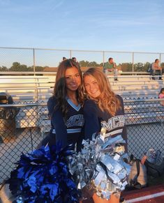 two cheerleaders posing for the camera at a football game