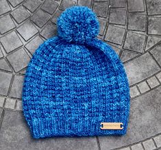 a blue knitted hat with a pom - pom on the top sitting on a cobblestone floor