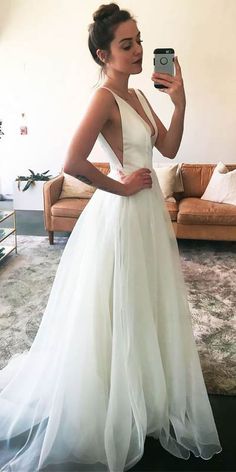 a woman in a white dress taking a selfie with her cell phone while standing next to a couch