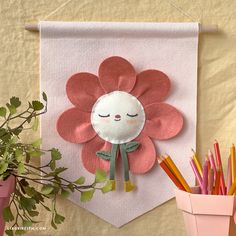 a paper flower hanging on a wall next to some pencils and flowers in a pot